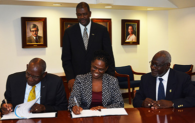 UVI President David Hall and Dr. Donna Powell Wilson, Council of Community Colleges of Jamaica executive director, sign a memorandum of understanding in the Administration and Conference Center on the St. Thomas Campus, while Dr. Haldane Davies, vice president for Business Development and Innovation, and Quince Francis, board chairman for the CCCJ look on. 